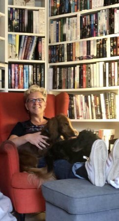 Me sitting in a red chair with my bookshelves behind me, and the dogs on my lap.