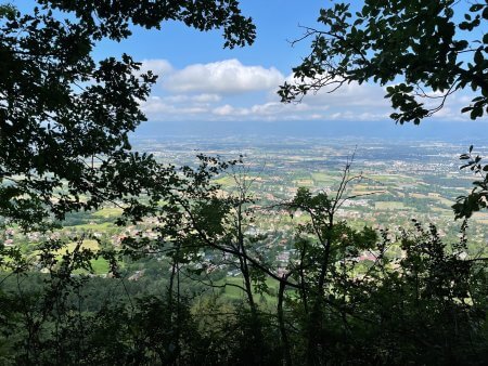 Trees in the foreground, in the background, blue sky and some clouds, and down there's a small village